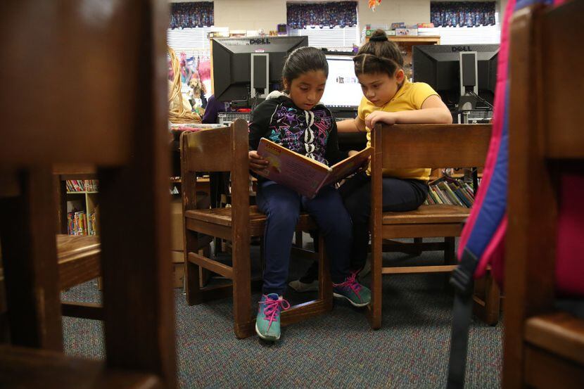 Second-grader Valerie Tovar (left) and first-grader Carla Chavez read a book in the library...