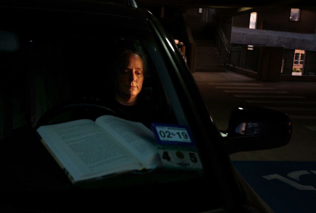 Katherine Rourke reads from the driver's seat of her station wagon where she also sleeps in...