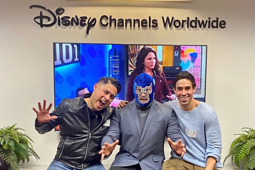 Foto de  Blue Demon Jr enseguida de dos actores enfrente de un anuncio que dice "Disney...