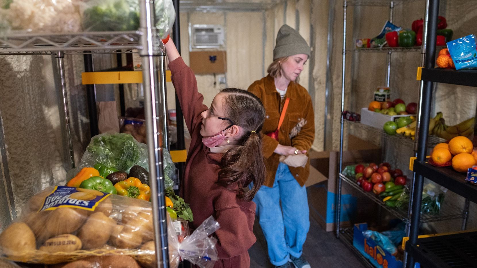 Finley Miles, 8, left, and her mother Hilary Miles, stock shelves with fruits and veggies...