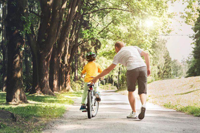 Un padre ayuda a su hijo aprender a usar una bicicleta.(GETTY PHOTOS)
