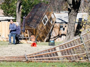 Homeowner Randy Popiel, front, walks by a damaged greenhouse sitting on the fence in the...