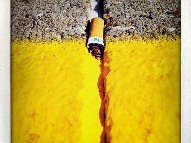 A Pall Mall cigarette lies discarded in a street crack, part of a series of photographs...
