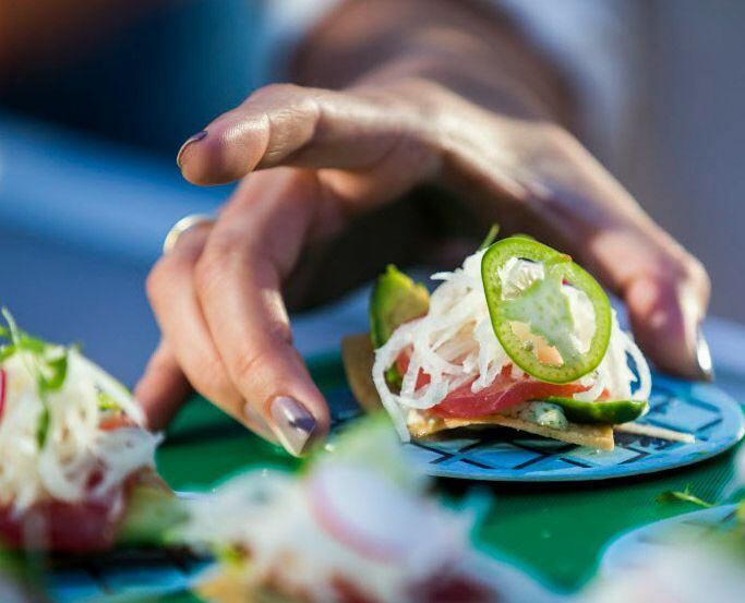 A woman reaches for a tuna tostada at a food-tasting event.