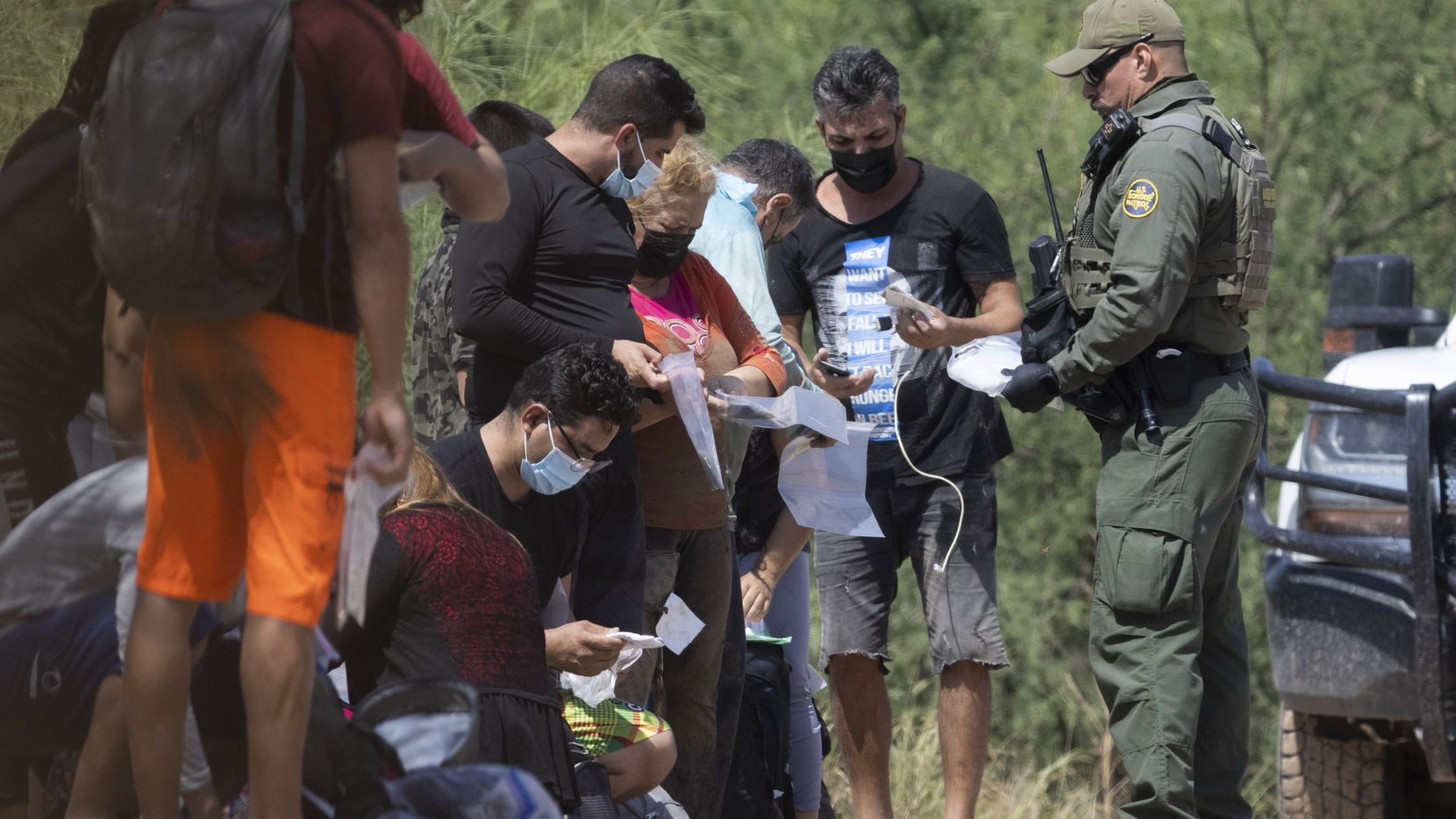 A group of mostly Cuban migrants are handed bags for their belongings by Border Patrol...