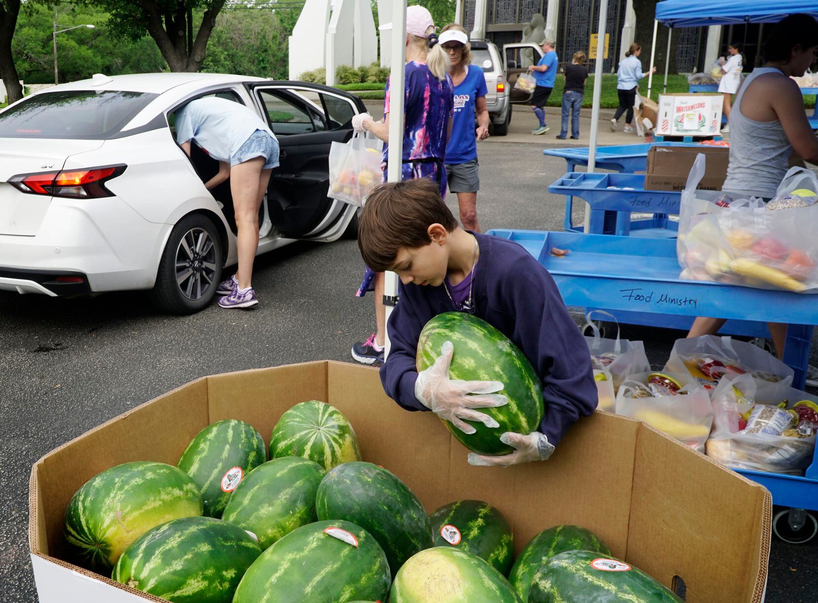 Jack Luth, 8, carries a watermelon to a car during a food giveaway at Lovers Lane United...