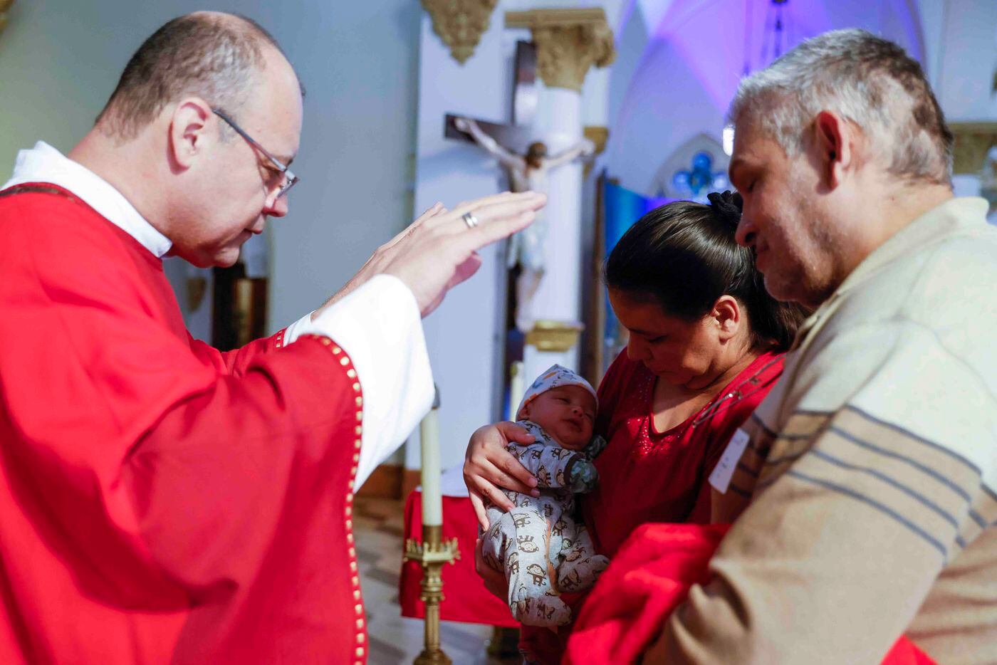 Decon Manuel Rendon, left, blesses three and half month old Ian Mendoza, carried accompanied...