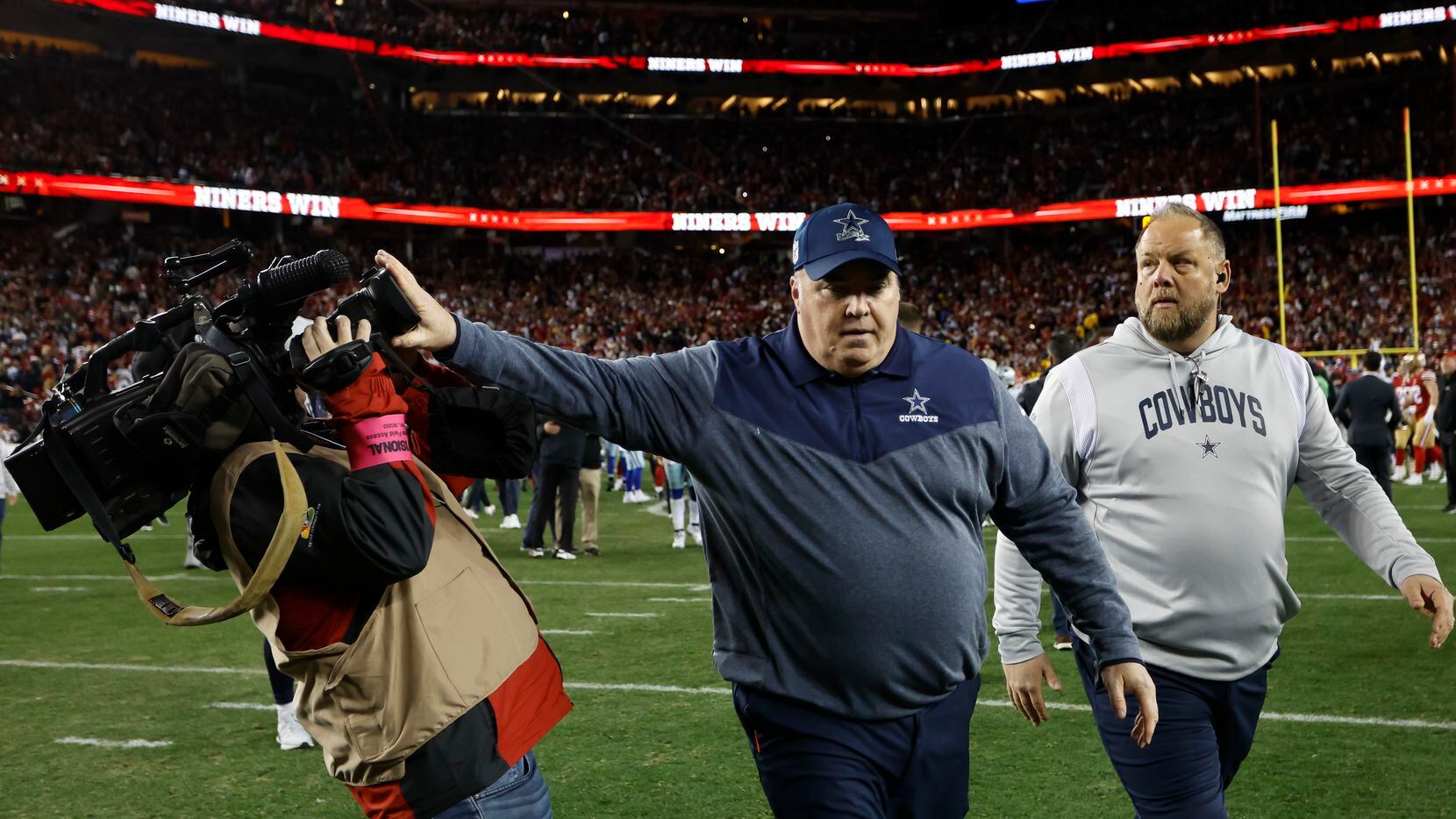 El entrenador en jefe de los Cowboys de Dallas, Mike McCarthy, empuja a un camarógrafo...