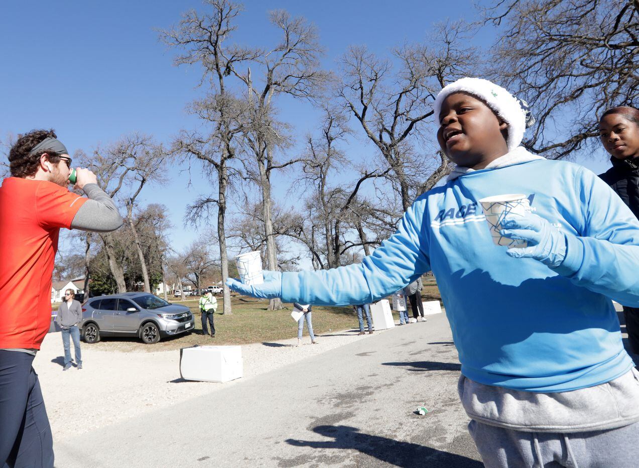 11-year-old Kristopher Williams, right, offers up refreshments as runners pass a water...