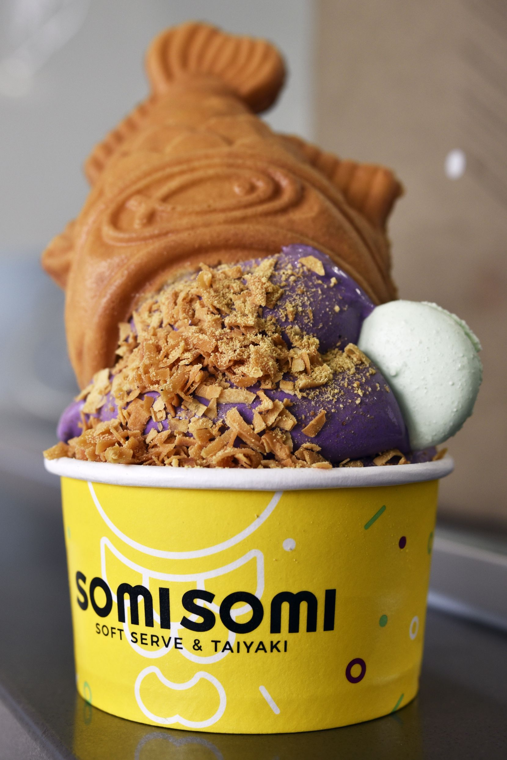 An upside down cone served in a cup with Ube flavored soft serve from SomiSomi Soft Serve &...