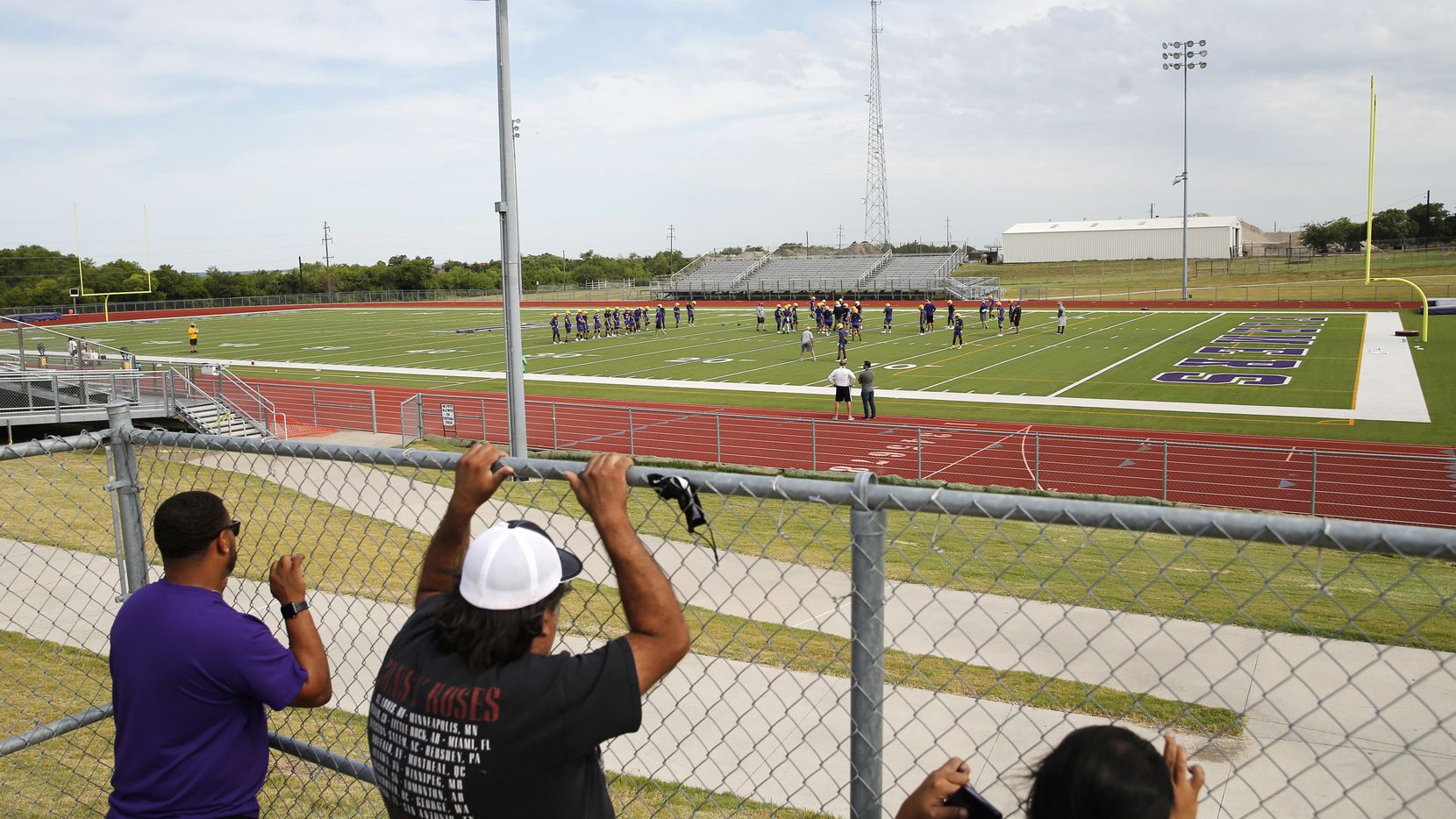 Parents of players Aaron Clark (left), Jose Chairez (center) and Corina Chairez (far right) watch practice from the gate during the first day of high school football practice for 4A's Farmersville High School in Farmersville, Texas on Monday, August 3, 2020. (Vernon Bryant/The Dallas Morning News)