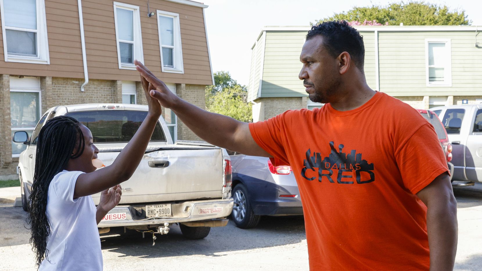 Kendall White, 10, high-fives Victor Alvelais of Dallas CRED while talking with residents of...