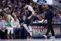 Dallas Mavericks' Luka Doncic slowly walks off the court with a staff member during the...