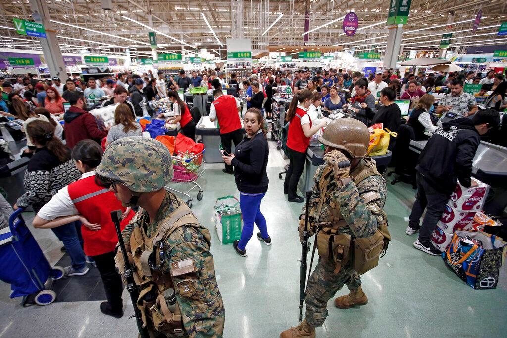 La policía militar hace guardia en un supermercado mientras los clientes pagan por sus...