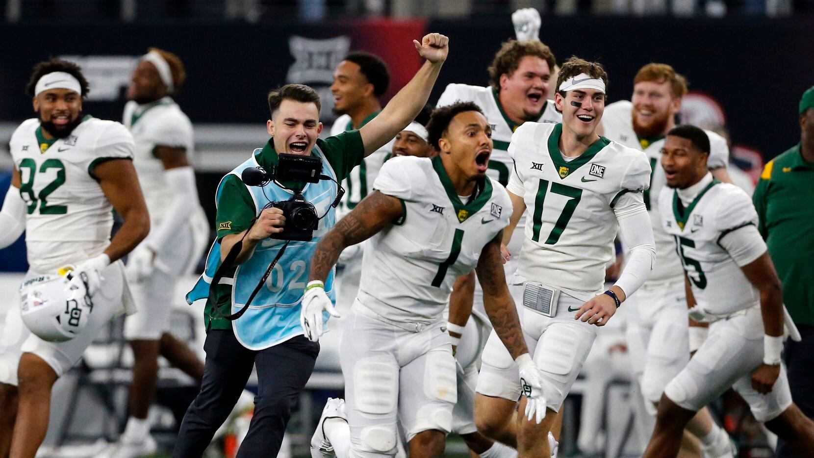 A school photographer (blue smock) celebrates with Baylor Bears running back Trestan Ebner (1) and the remainder of the Baylor bench at the end of  the Big 12 Championship football game against Oklahoma State at AT&T Stadium in Arlington on Saturday, December 4, 2021. Baylor won 21-16.