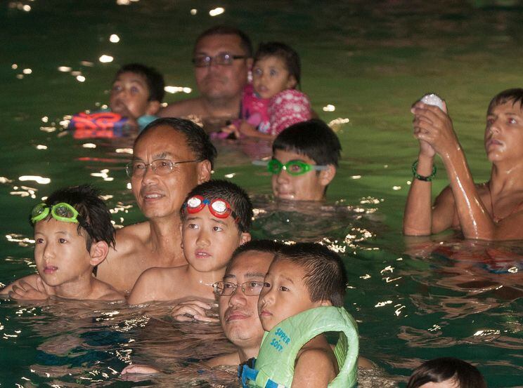 Families watch a movie from a swimming pool. 