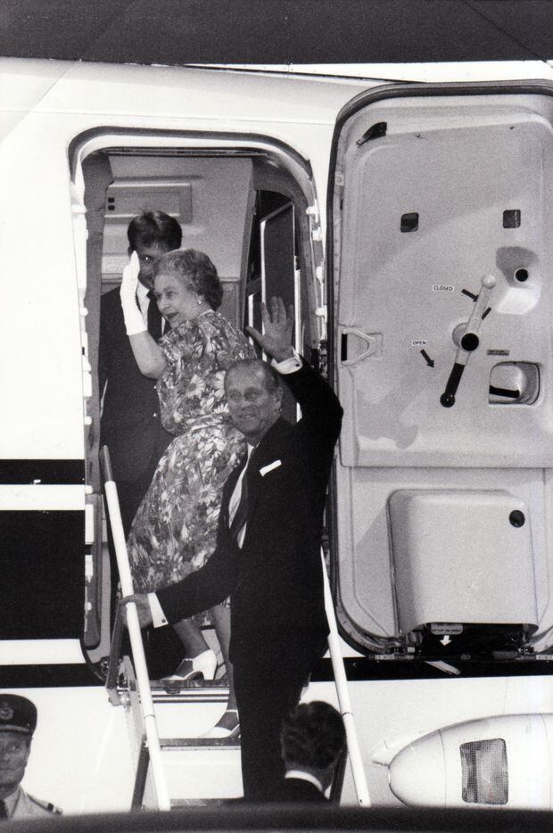 Queen Elizabeth II and Prince Philip wave goodbye as they climb aboard a plane at the end of...