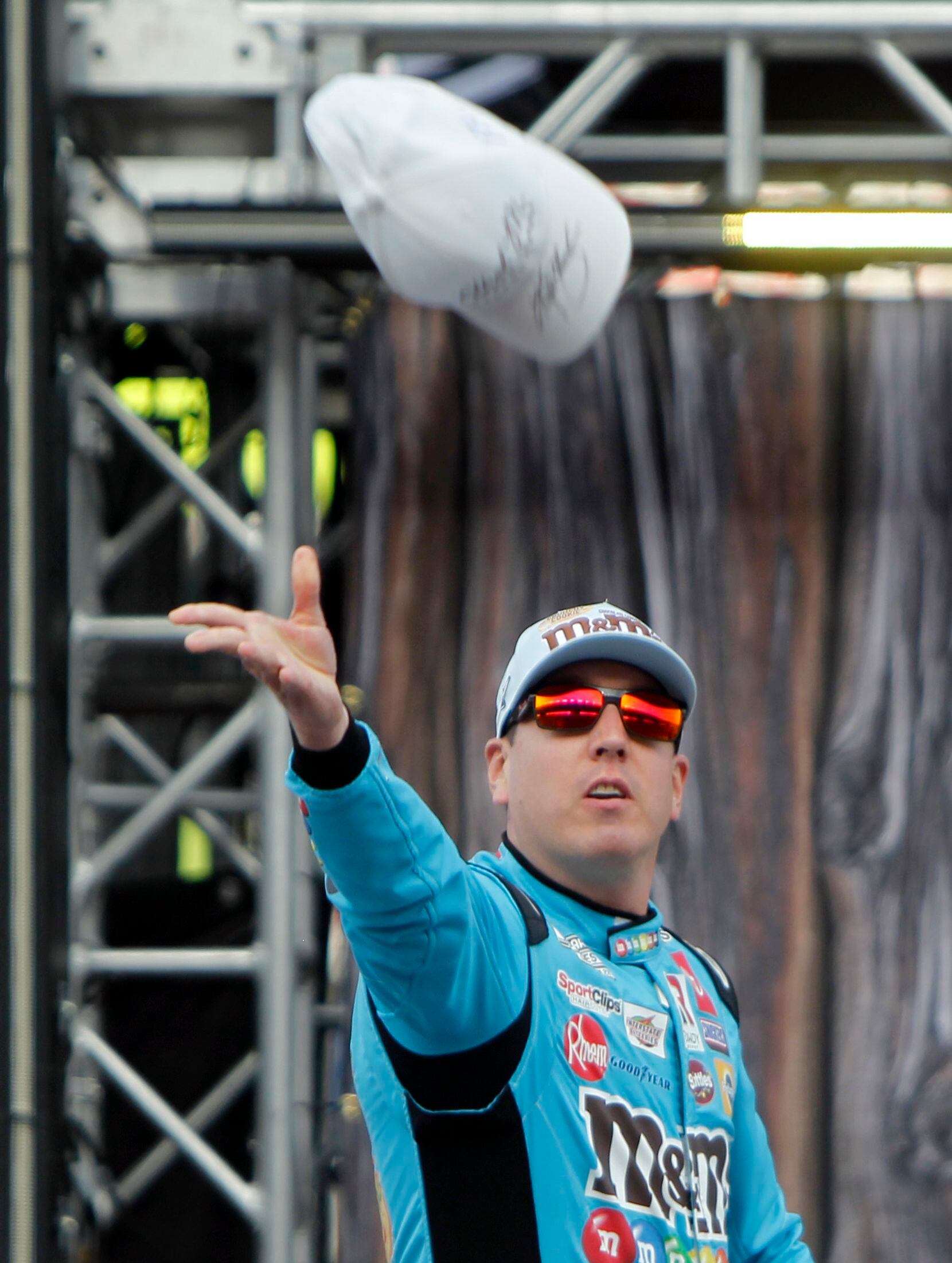 Kyle Busch, driver of the #18 M&M's Crunchy Cookie Toyota tosses an autographed cap toward a...