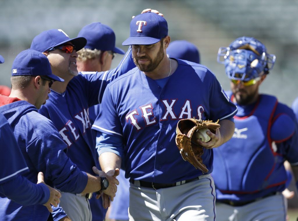 Texas Rangers pitcher Colby Lewis, center, walks off the field with teammates at the end of...
