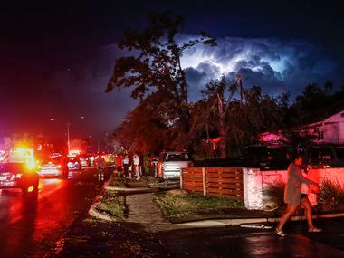 Lightning and emergency lights highlight damage as people gather in the parking lot of a...