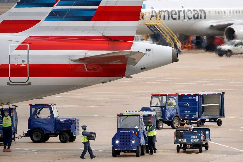 American Airlines crew members move luggage from an aircraft onto carts at Dallas-Fort Worth...