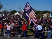 A large flag dons the likeness of former President Donald Trump as people gather at Waco...