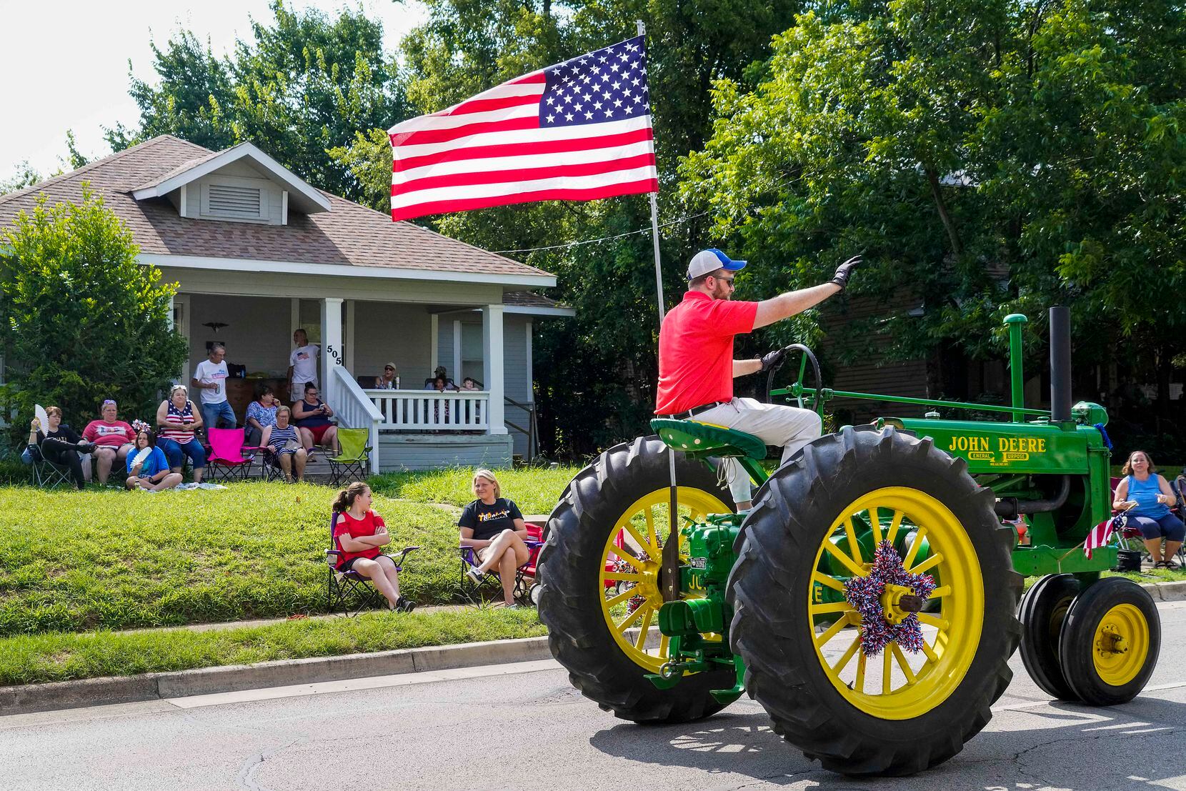 A man riding tall on a John Deere tractor waved to residents along the route of the Arlington Independence Day Parade on July 5. The parade, the city’s longest running event, had been canceled in 2020 due to the pandemic.
