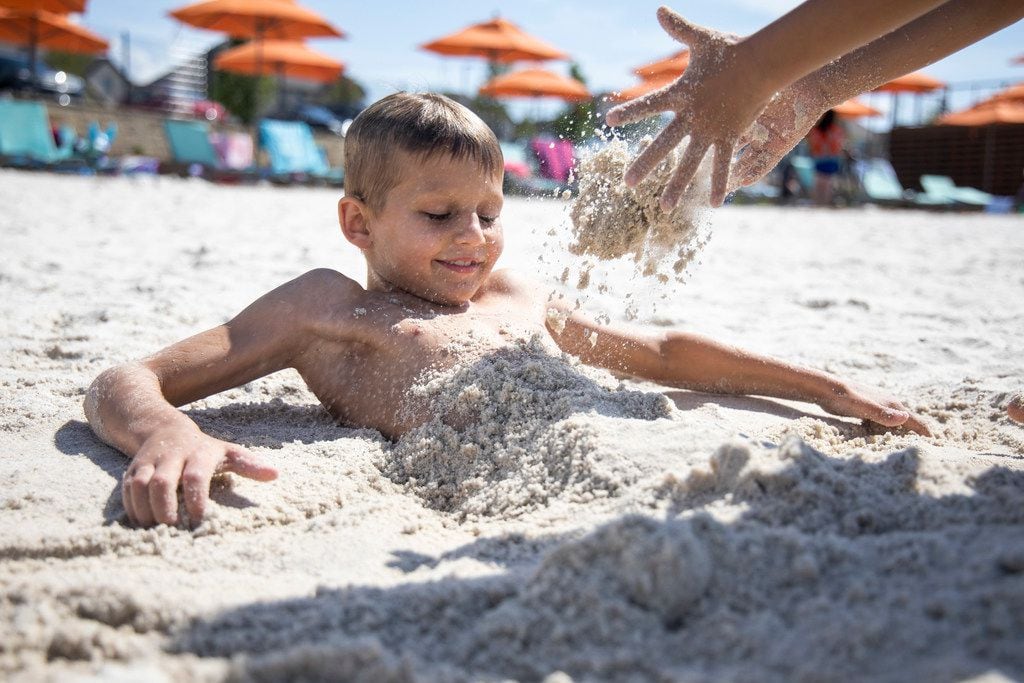 Cooper Dalby, 10, watches as Rice Lee, 7, buries him in the sand on the beach alongside the...
