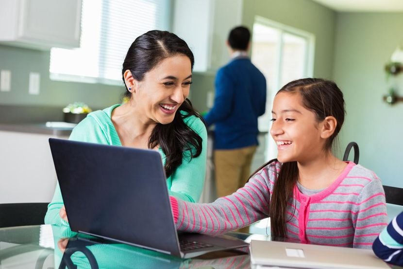 Una madre ayuda a su hija con tareas escolares en una computadora laptop.(GGETTY IMAGES)
