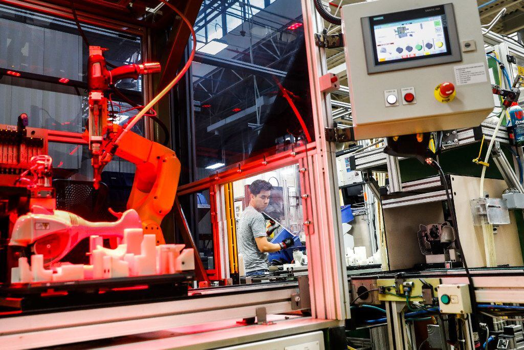 IAn assembly line laborer works alongside a collaborative robot, left, on a chainsaw...