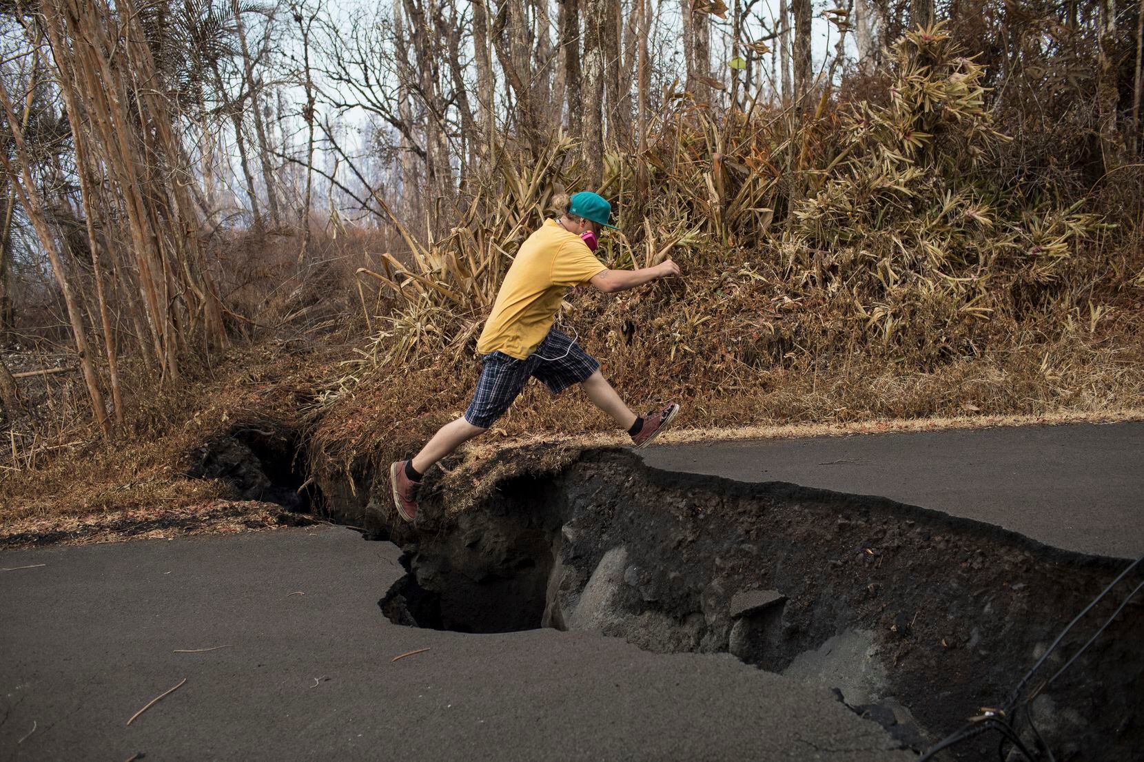 Brandon Lofgreen leaps across a large crack in a road in the Leilani Estates neighborhood,...