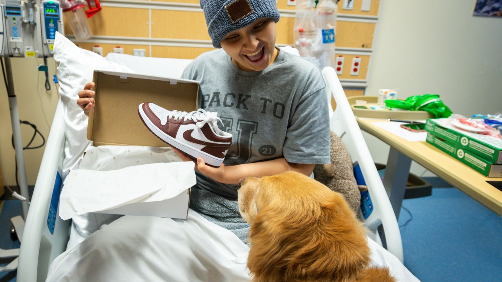 Un paciente de Children's Health Dallas muestra zapatos deportivos nuevos al perro de...