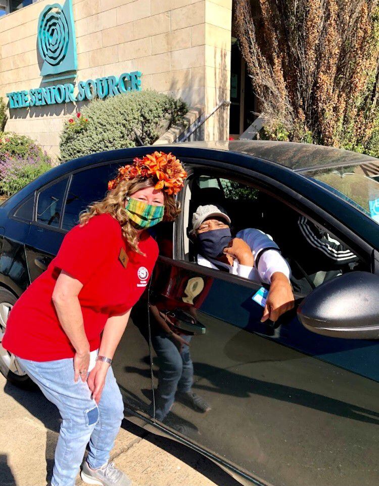 A Senior Source employee in a red shirt wearing a mask poses outside of a car where a...