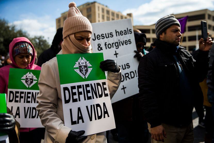 Julia Montiel (center) and other demonstrators pray and hold signs at a rally after marching...