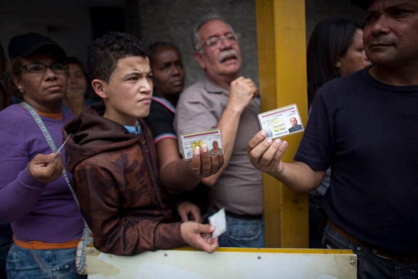 Residentes de Caracas muestran sus credenciales de identificación mientras hacen fila para...