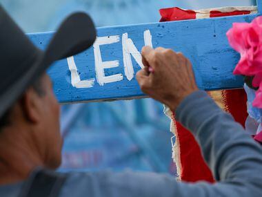 Artist Roberto Márquez paints the name of Len Root, one of three identified victims of the...