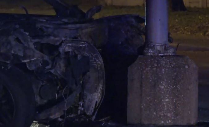 The charred remains of a car rest against a light pole after a crash that killed two people...