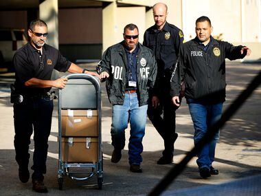 Dallas police officials cart out boxes from a raid on the Catholic Diocese of Dallas,...