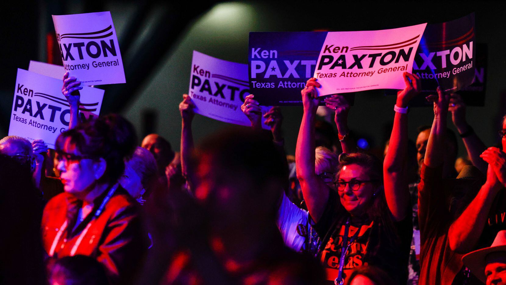 Attendees show Ken Paxton's signs as he gives a speech during a general meeting as part of...