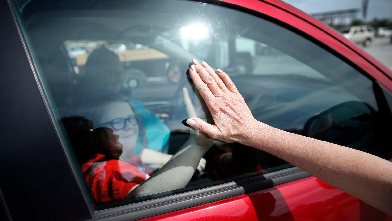 Volunteer Karen Kirk, of Houston, gives a student a high-five through the window after a drive-through meal pickup outside AT&T Stadium in Arlington, Texas, March 28, 2020. Arlington Charities, Fielder Road Baptist Church and Tarrant Area Food Bank volunteers loaded school parents' vehicles with weekend meals for Arlington ISD families.