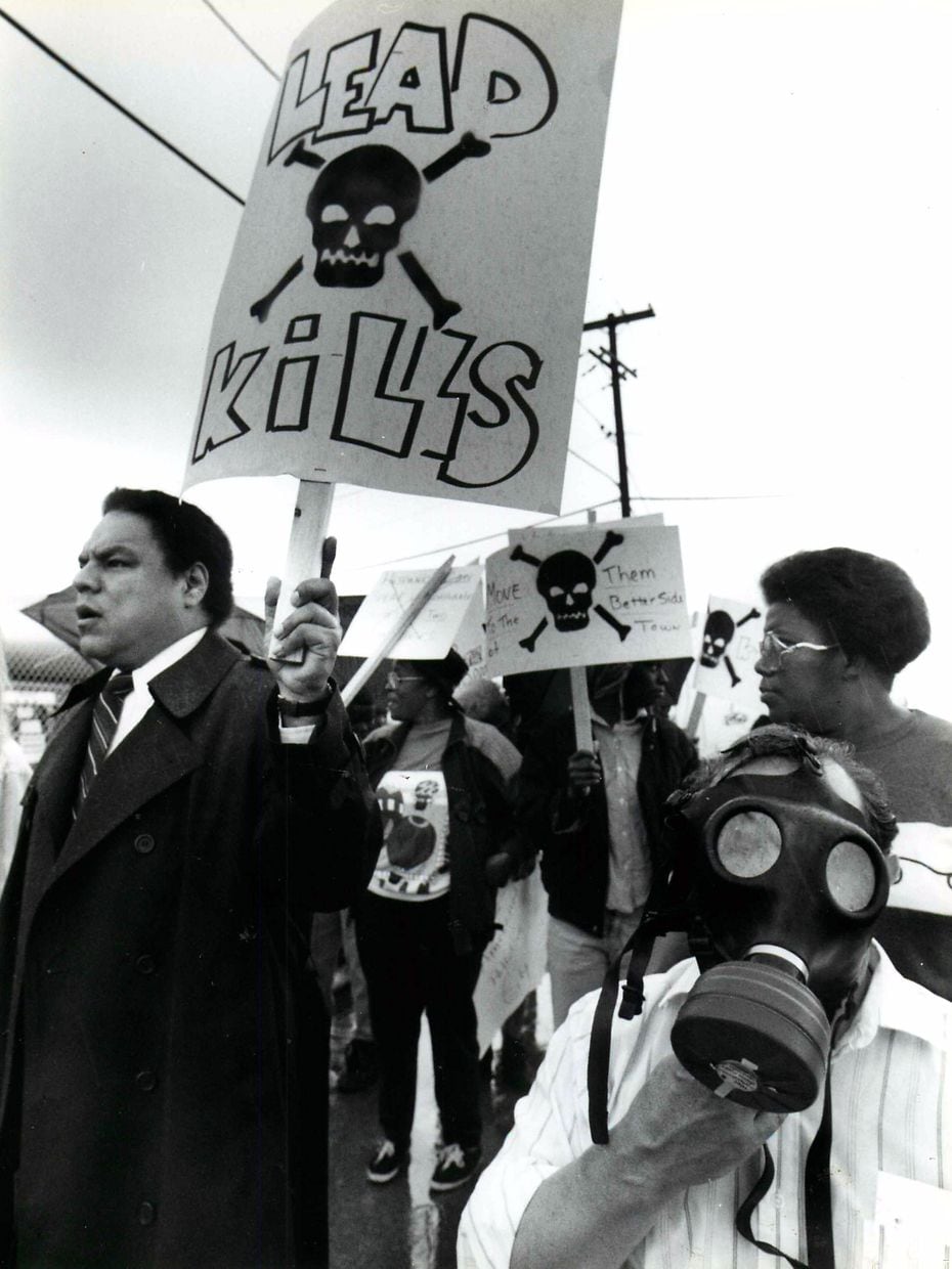 In March 1991, protestors march past industrial sites on Singleton Boulevard in West Dallas to call attention to pollution in their neighborhood.  At left, holding sign, is Ricardo Medrano.  At right, wearing gas mask, is Luis Sepulveda. (Ira Rosenberg)
