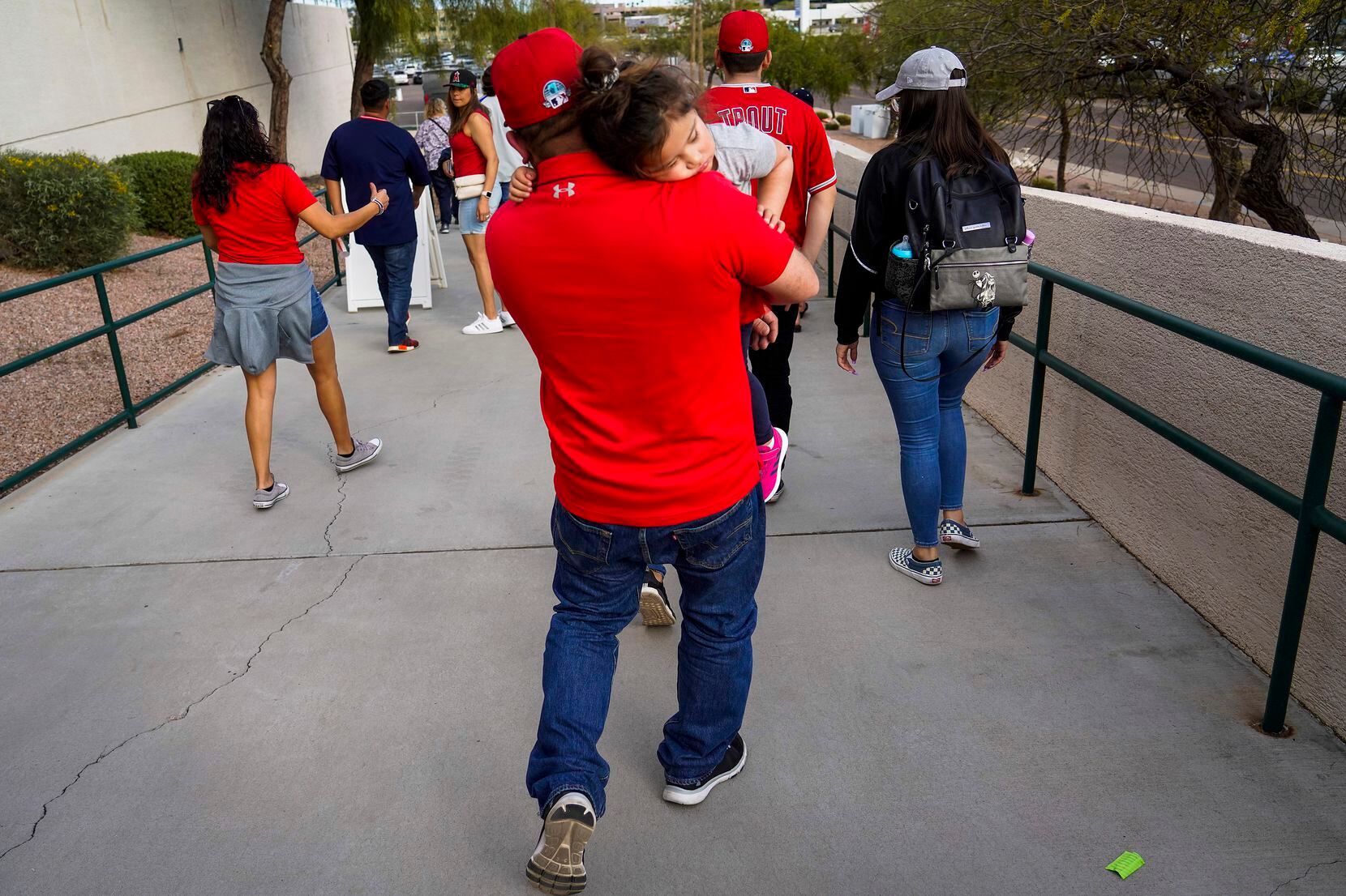A Los Angeles Angels fan carries a sleeping baby as they depart the stadium after victory...