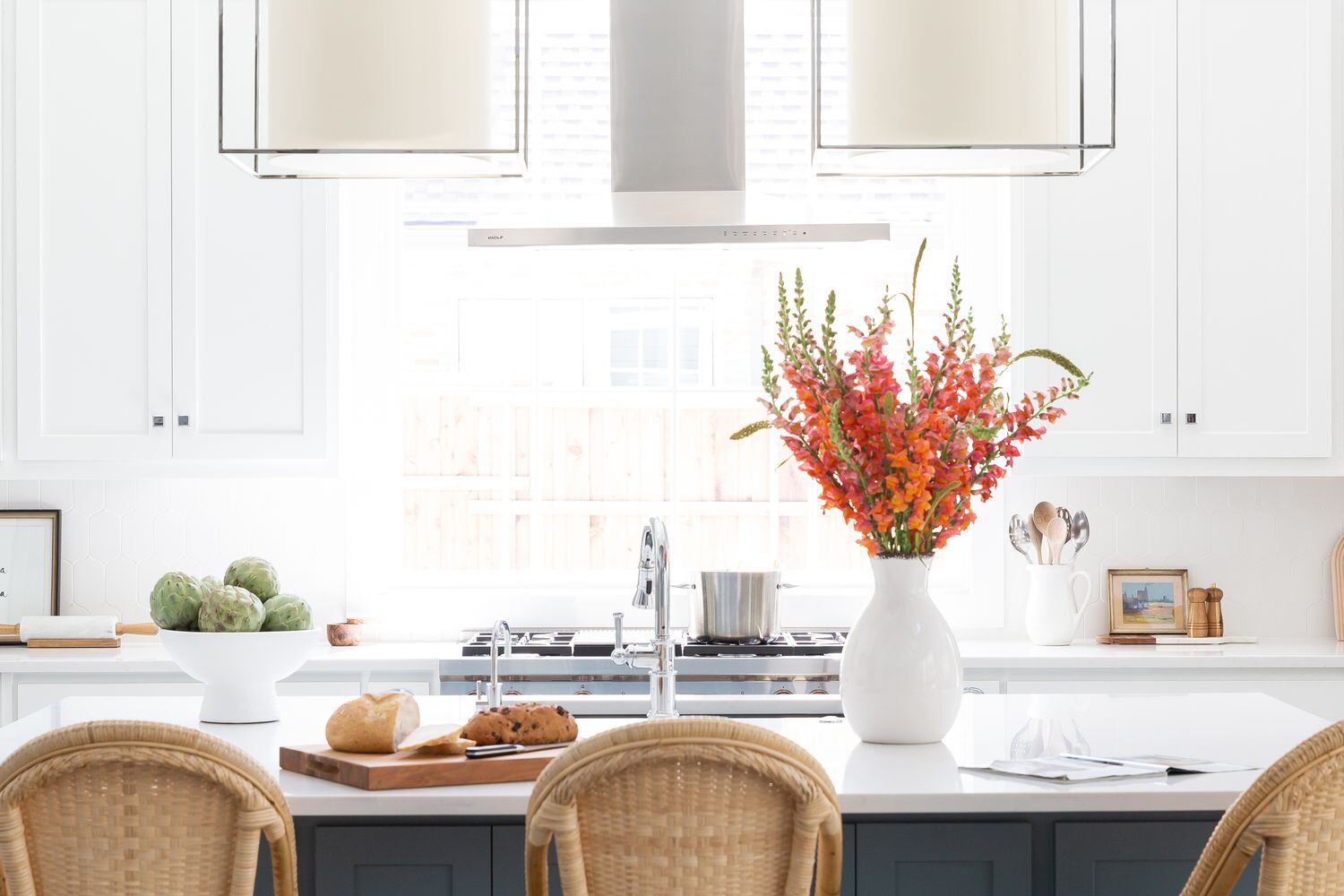 A thin, modern vent hood allows natural light to flow into a white kitchen with orange...