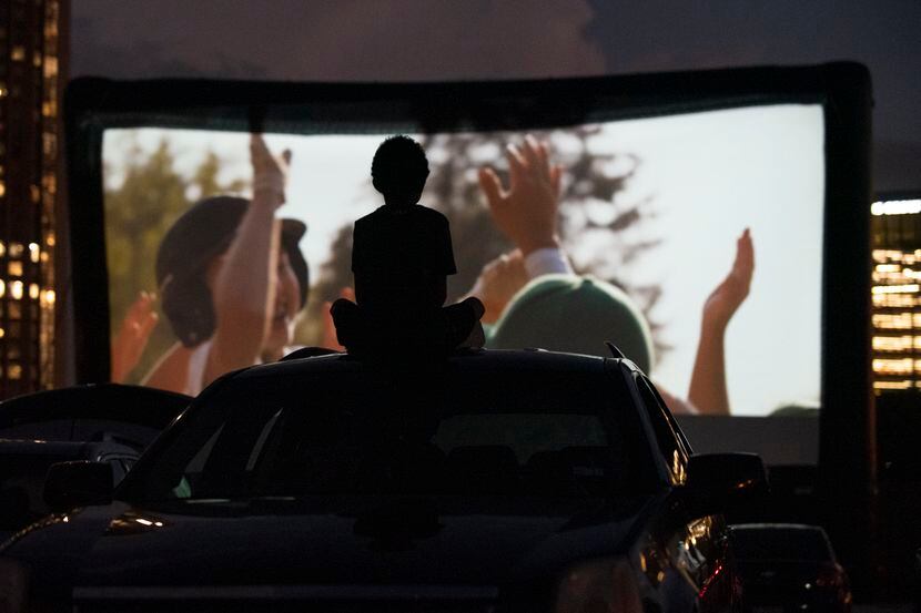 A boy sits atop the roof of an SUV while watching a movie at Rooftop Cinema Club drive-in,...
