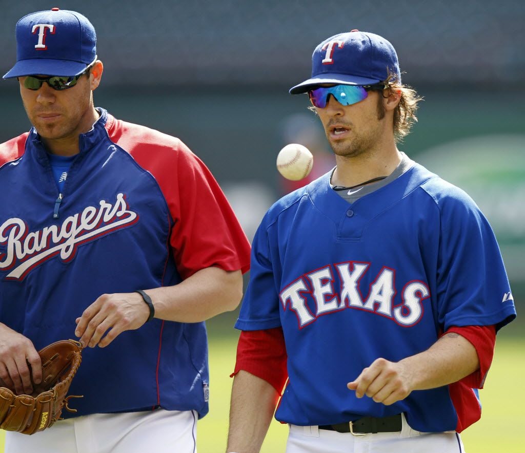 Texas Rangers pitcher C.J. Wilson tosses a ball as he walks with Colby Lewis during practice...