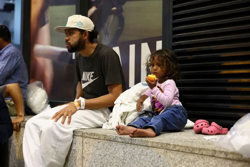 Cataleya takes a bite of a nectarine alongside her father Elier as they wait for a bus to...