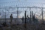 A Texas National Guard soldier escorts migrants back south behind a razor wire barrier on...
