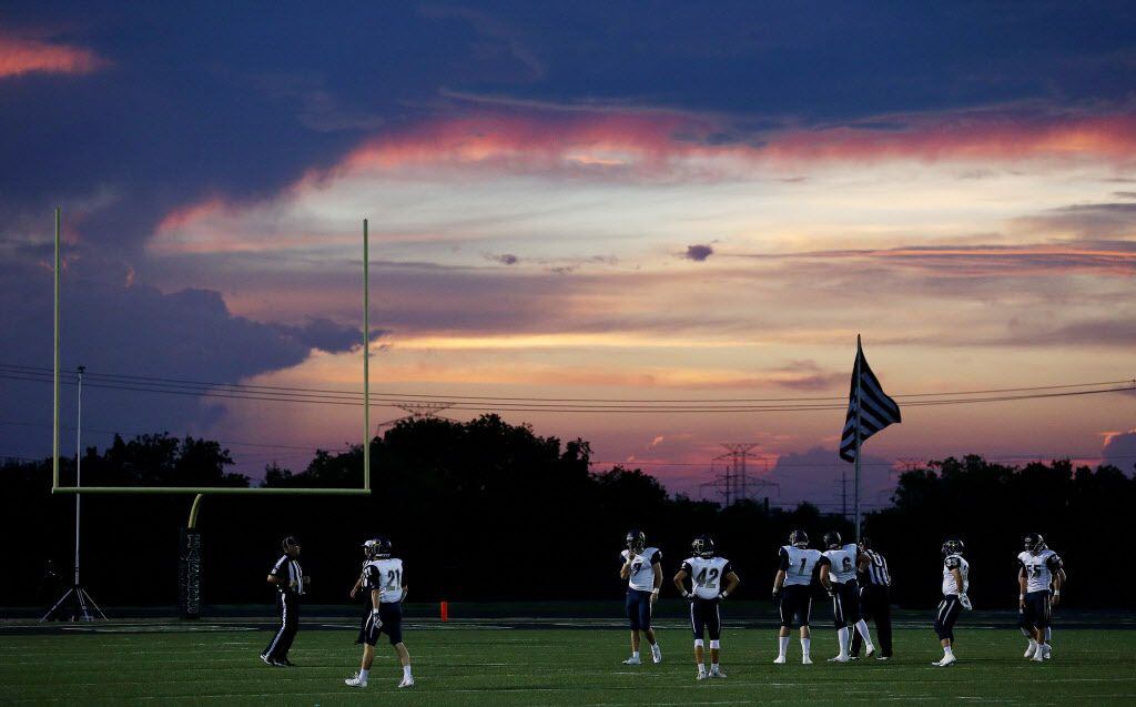 Jesuit players wait for the play to resume as the sun falls during a high school football...