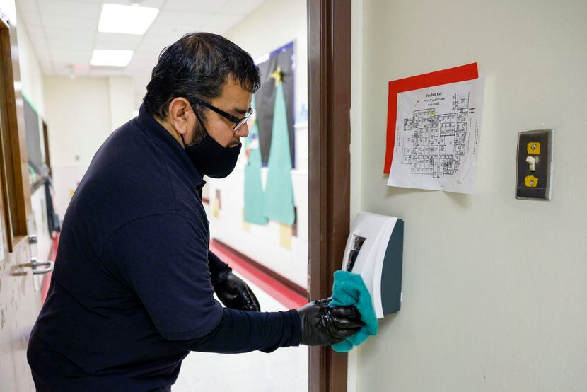 Joe Gomez wipes down a hand sanitizer dispenser at Rayburn Elementary STEAM Academy in Grand...
