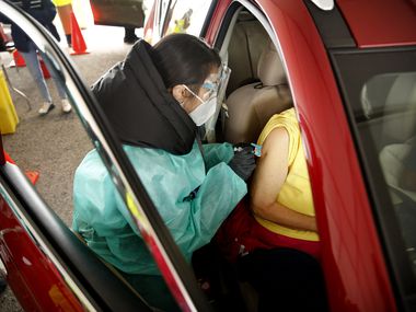 A senior receives a COVID-19 vaccination from a volunteer working the drive-thru line at Fair Park in Dallas, Wednesday, February 10, 2021.